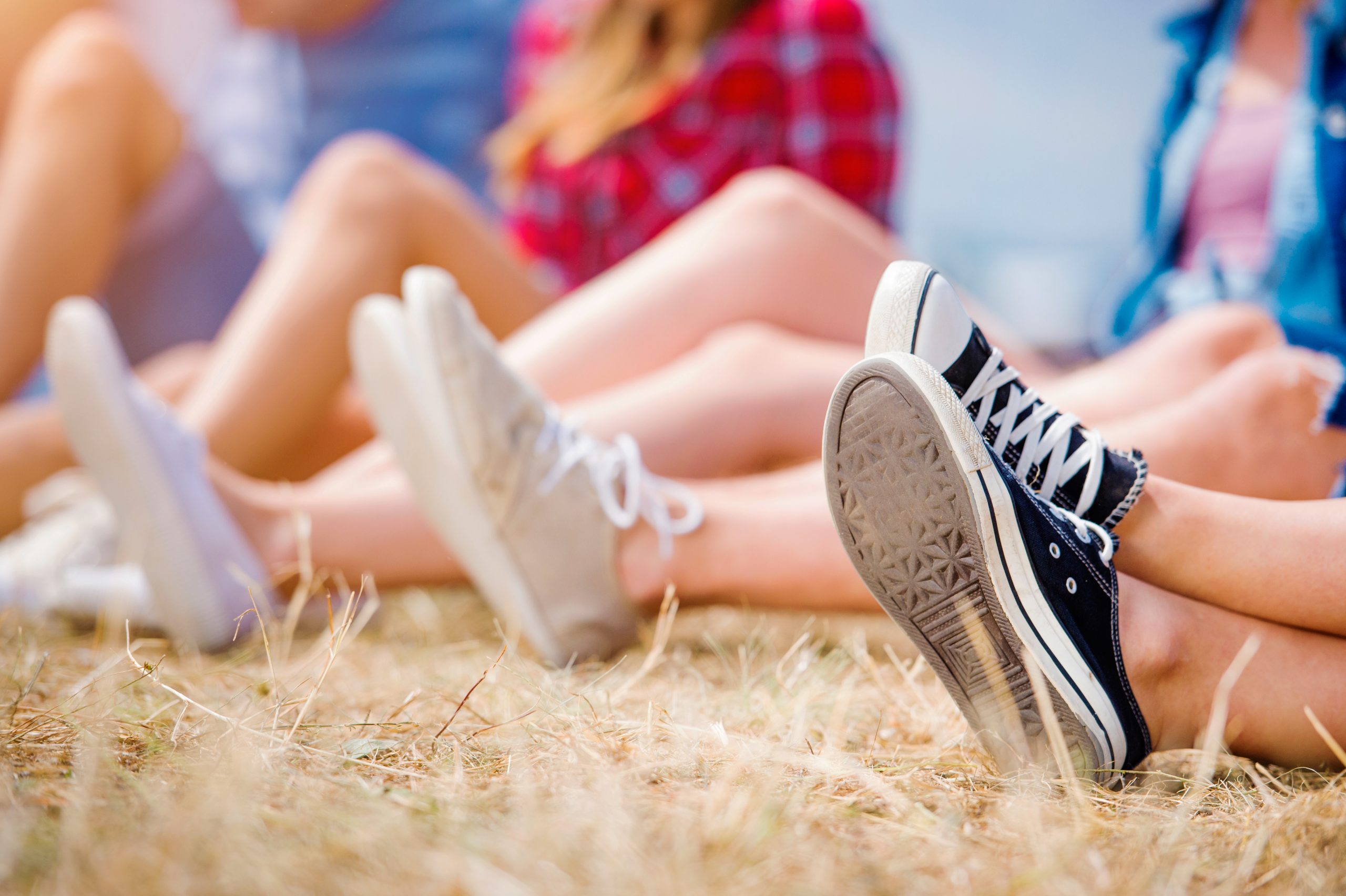 legs-of-teenagers-at-summer-music-festival-canvas-shoes-sitting-on-the-grass-in-front-SBI-305195361-scaled-1